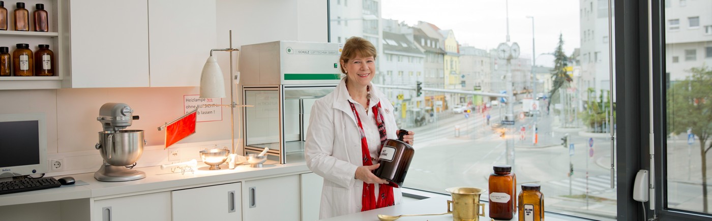 Mag Christiana Seidl im Labor, lächelnd. Im Hintergrund sieht man durch das Panoramafenster den Kagranerplatz